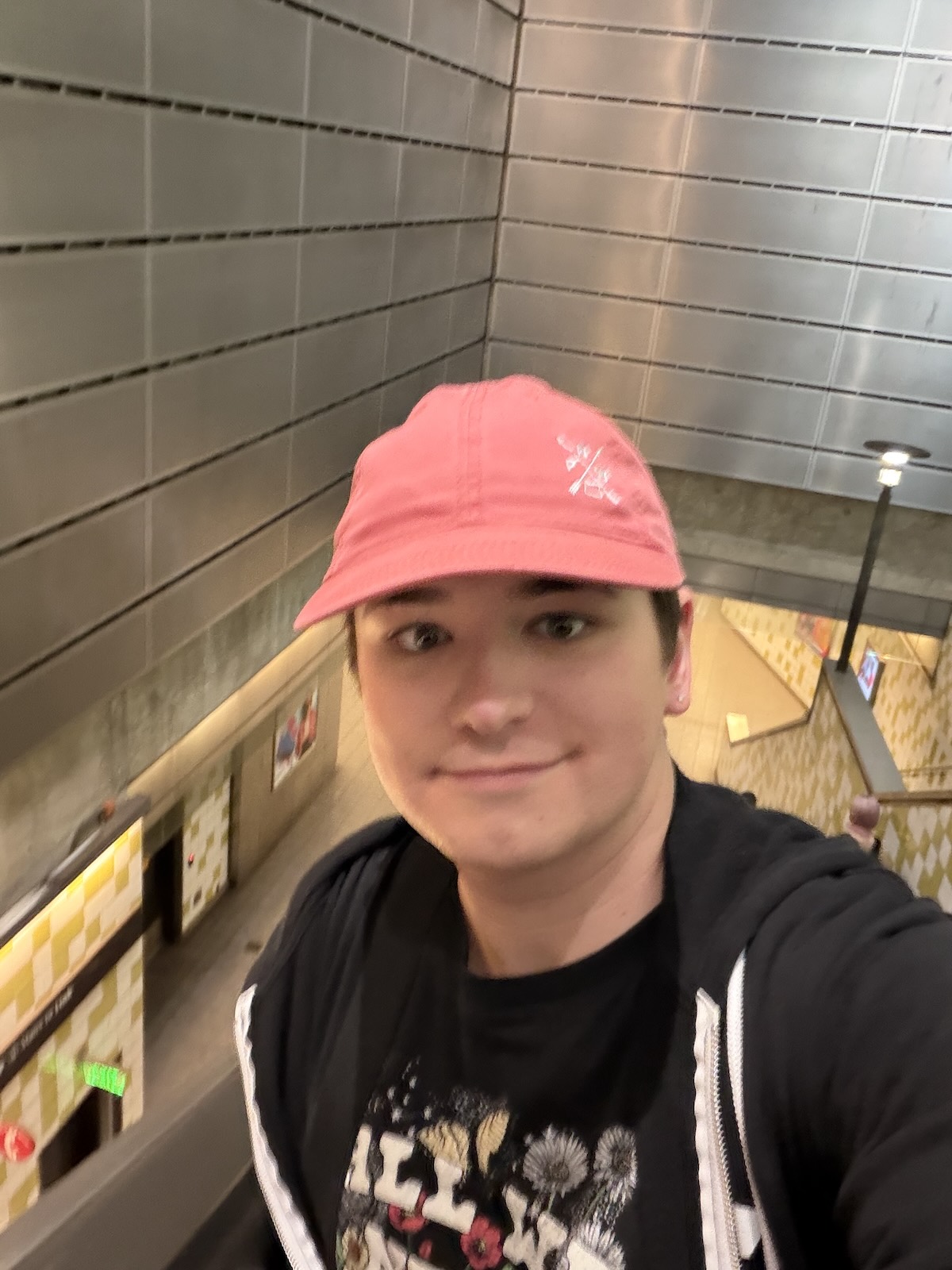 A photo of Brittany in a black tshirt and pink hat ascending an escalator in a transit station.